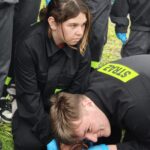 młodzież w strojach straży pochylona nad poszkodowanym