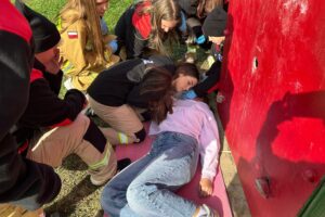 dziewczynka leży na macie pod ścianką, obok młode osoby ze straży