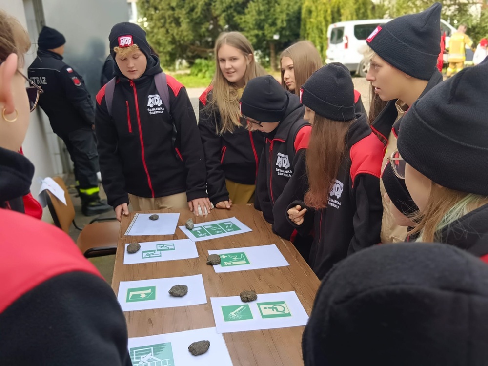 Młodzież przy stole, a na stole leżą znaki ewakuacji