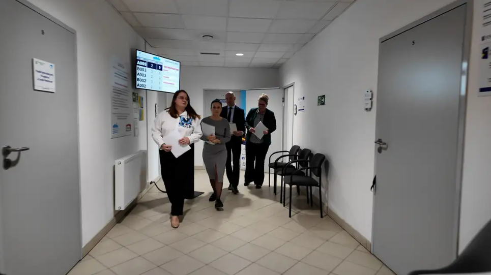 ludzie idą korytarzem, po bokach szare drzwi