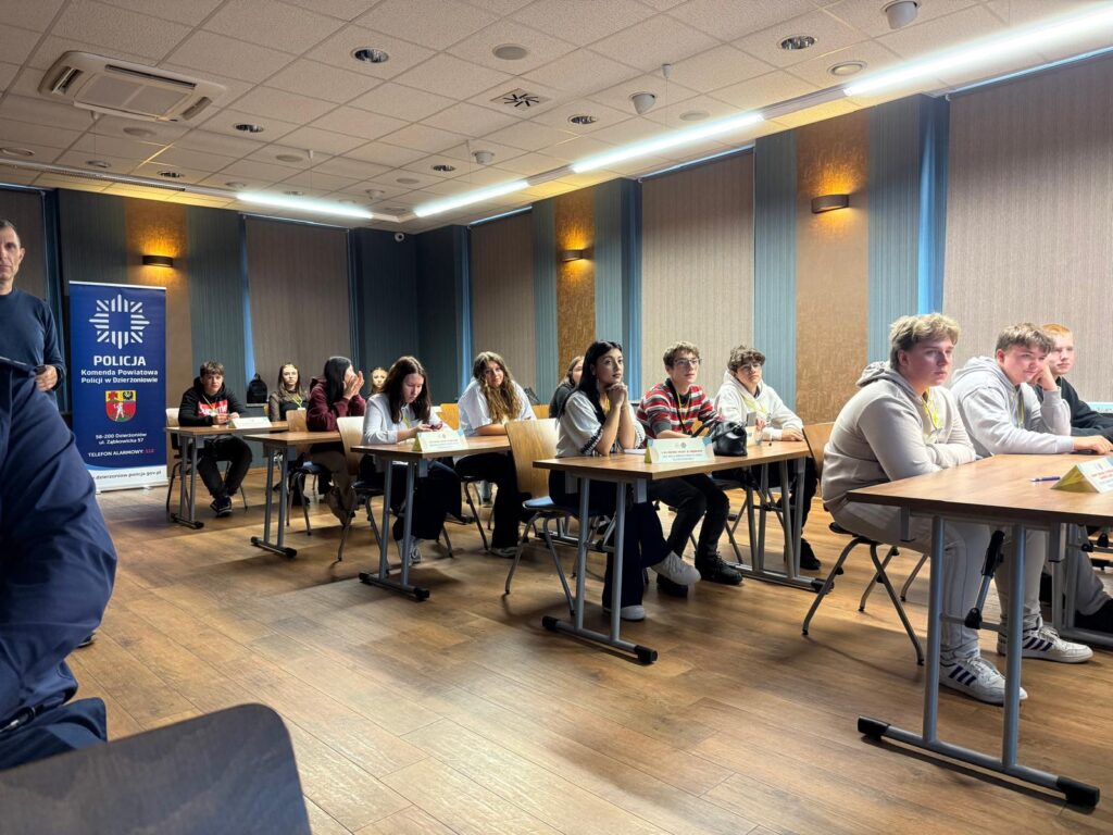 młodzież siedzi na sali w ławkach