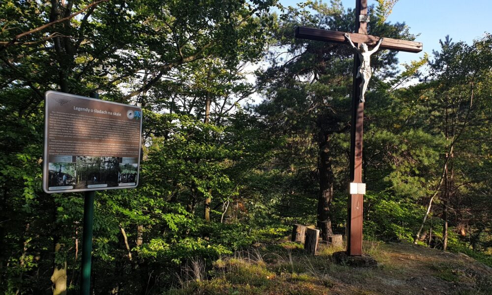 krzyż na górze, obok tablica, w tle drzewa