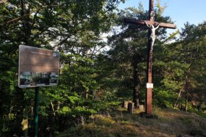 krzyż na górze, obok tablica, w tle drzewa