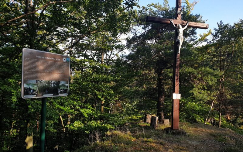 krzyż na górze, obok tablica, w tle drzewa