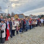 ludzie z kwiatami pod pomnikiem