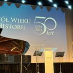 widok na scenę, fortepian, mikrofony, mównica, na ekranie napis 50 lat