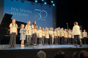 dzieci i młodzież na scenie w dużej grupie śpiewają