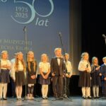 dzieci stoją na scenie i śpiewają