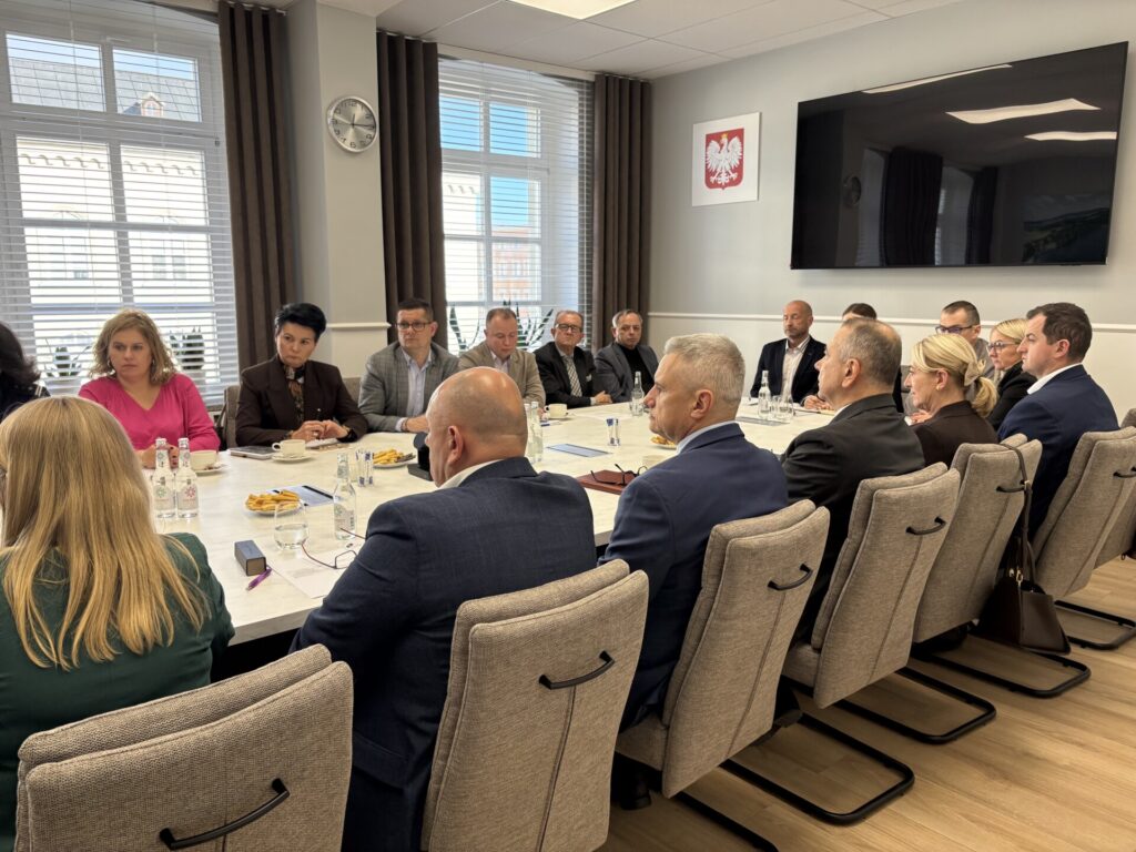 członkowie komisji siedzą przy stole, w tle okna