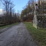 droga w stronę lasu, po prawej stronie kamienny budynek z oznaczeniem szlaku