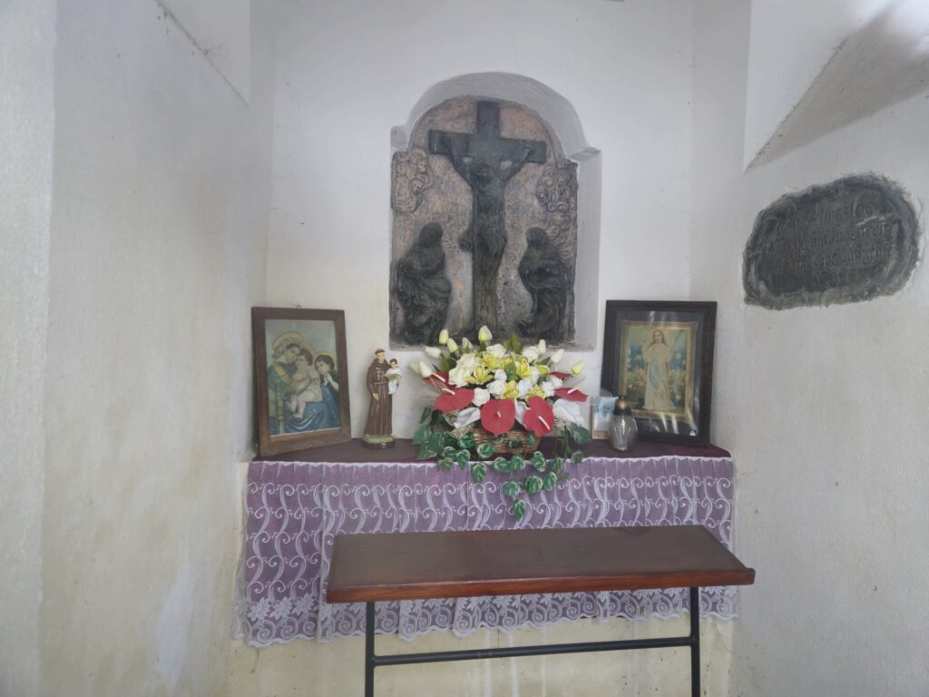 widok wewnątrz kapliczki, mały ołtarzyk, a ponad nim płaskorzeźba ukrzyżowania