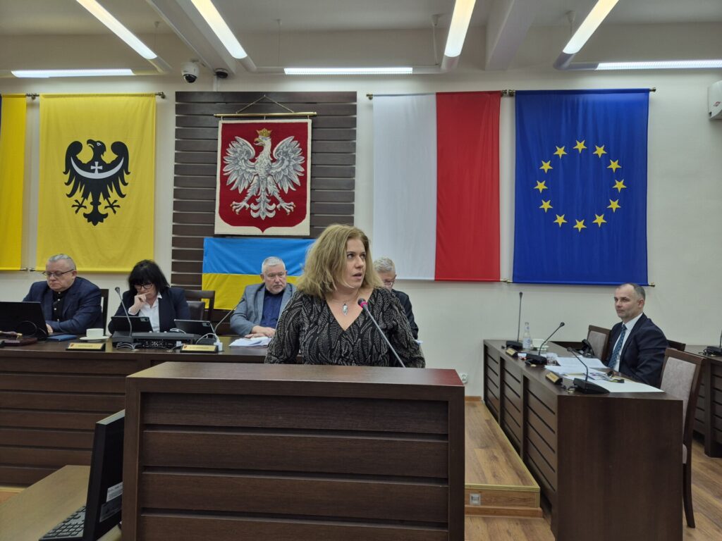 prokurator przemawia z mównicy, w tle prezydium rady