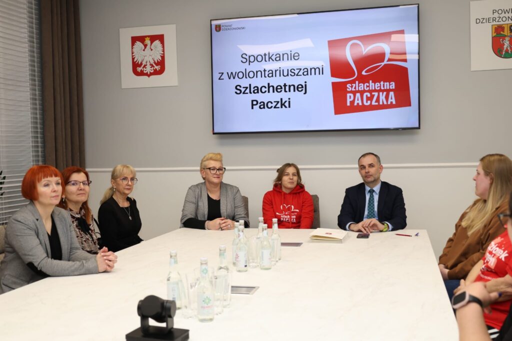 wolontariusze siedzą przy wspólnym stole z wicestarostą i członkiem zarządu powiatu