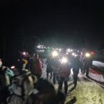 grupa ludzi idzie po śniegu z latarkami czołowymi