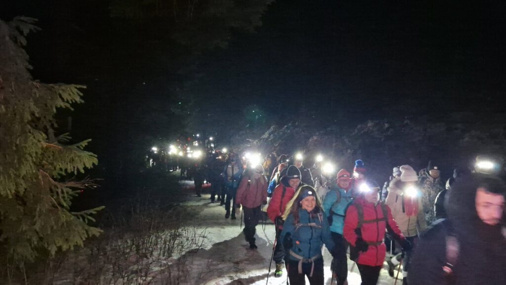 ludzie idą po śniegu wspólnie z latarkami