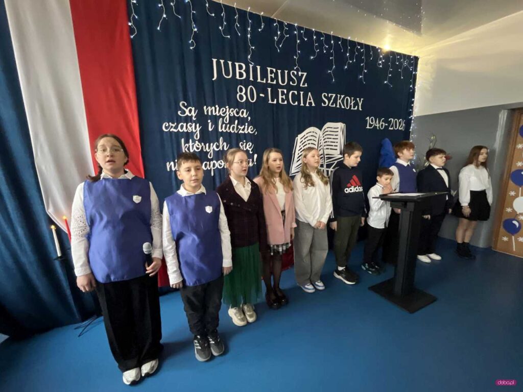 dzieci na scenie występują, w tle 80-lecie szkoły