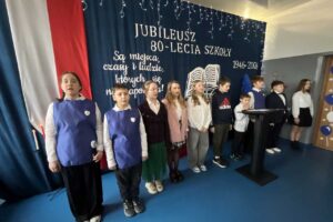 dzieci na scenie występują, w tle 80-lecie szkoły