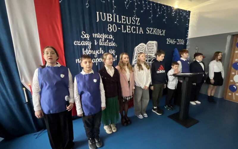 dzieci na scenie występują, w tle 80-lecie szkoły