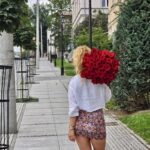 zdjęcie przedstawia kobietę z bukietem róż idącą ulicą