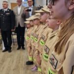 młodzież w strojach strażackich, w tle samorządowcy i komendanci