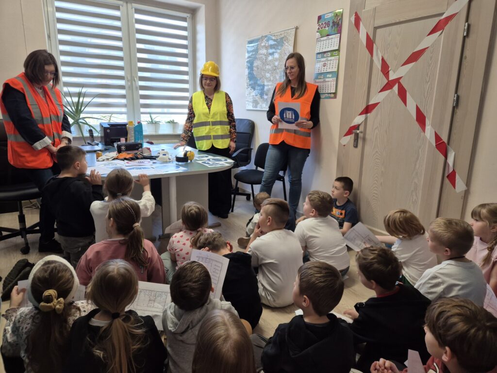 pracownice sanepidu w odblaskowych kamizelkach pokazują dzieciom znaki