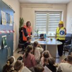 pracownice sanepidu w odblaskowych kamizelkach pokazują dzieciom znaki
