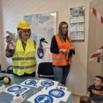 pracownice sanepidu w odblaskowych kamizelkach pokazują dzieciom znaki