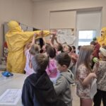 pracownik sanepidu w żółtym kombinezonie z grupa dzieci