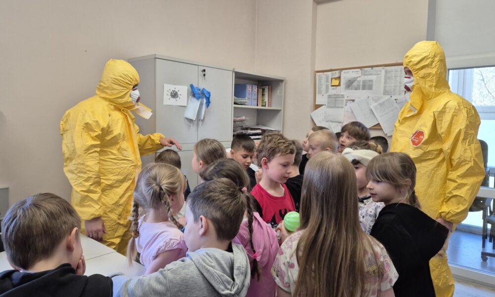 pracownicy sanepidu w żółtych kombinezonach z grupą dzieci