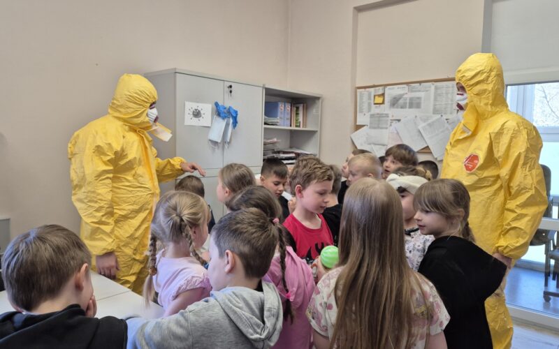 pracownicy sanepidu w żółtych kombinezonach z grupą dzieci