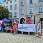 dwie kobiety w kapeluszach na scenie, 2 mężczyzn trzyma baner