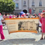 dwie kobiety w kapeluszach trzymają baner Dzienny Dom Senior +