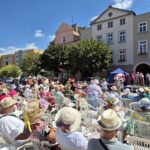 duża grupa ludzi siedzą na krzesłach plastikowych w kapeluszach przed sceną