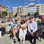wicemarszałek, poseł i wicestarosta w kapeluszach siedzą na ławce, w tle inni ludzie w kapeluszach