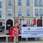 poseł na scenie przed ratuszem, obok kobiety w kapeluszu