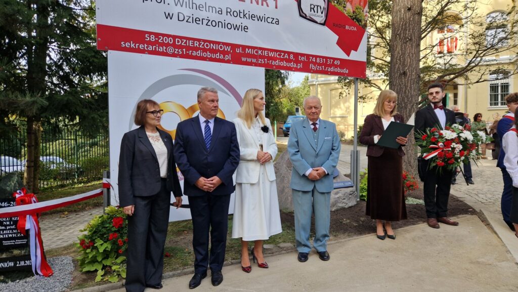 grupa osób pod banerem z nazwą szkoły