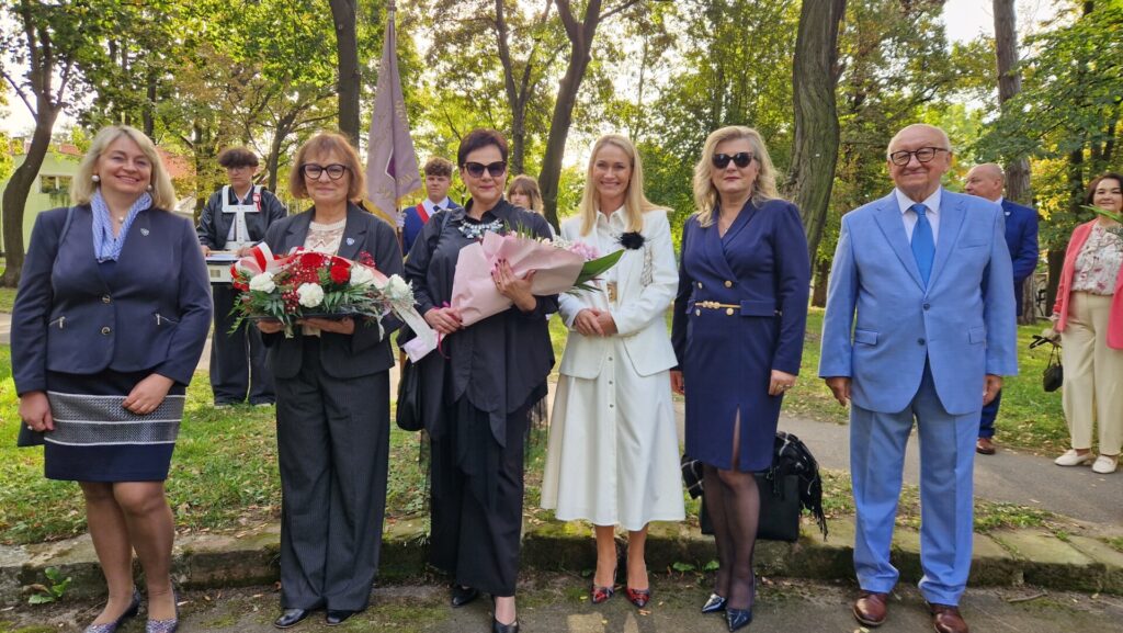 grupa ludzi z kwiatami w parku przy pomniku
